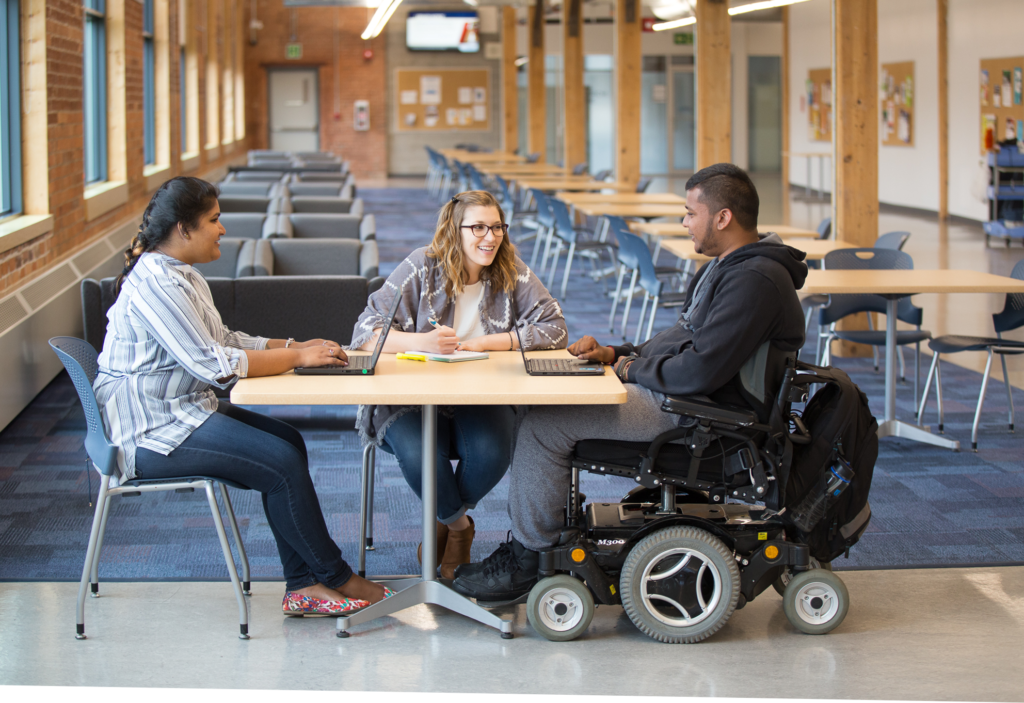 Trois étudiants dont un en chaise roulante dans une cafétéria universitaire